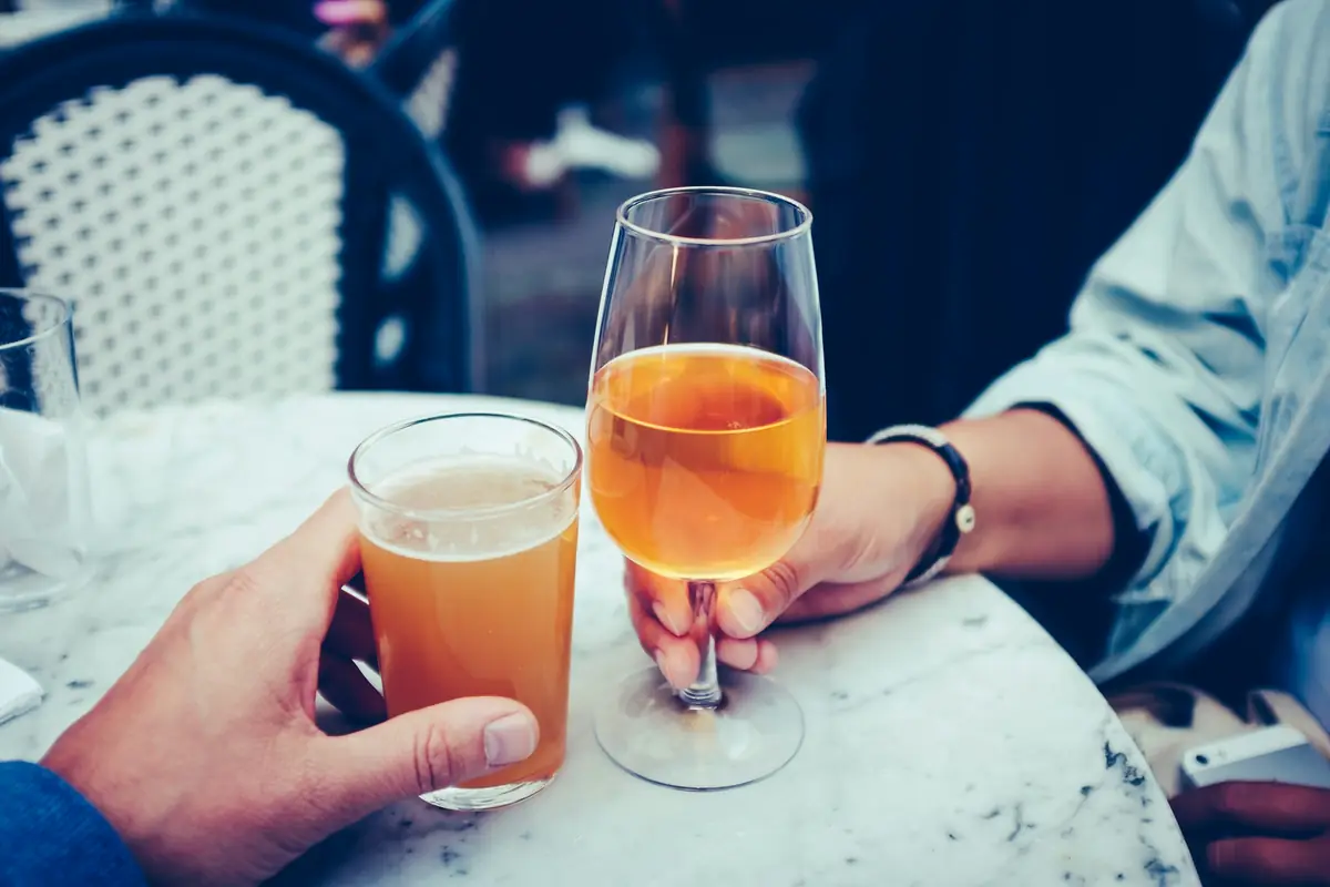 Two hands raising glasses of orange wine across a marble table