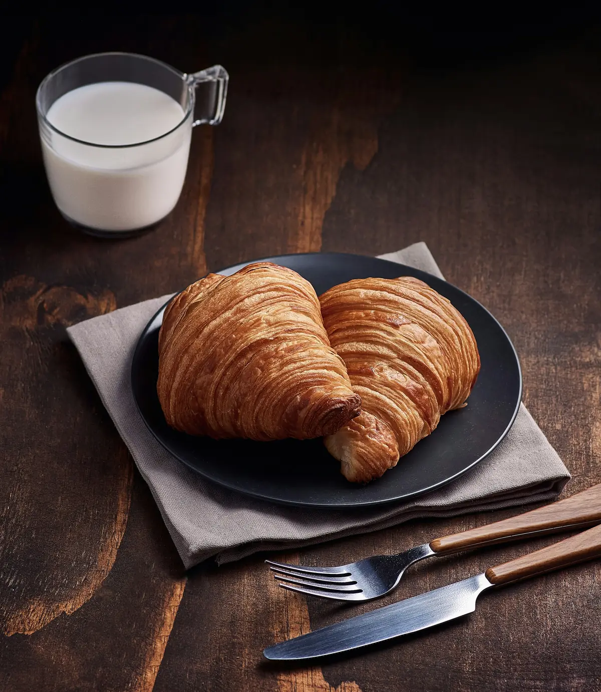 Croissants on a dark plate beside a glass of milk