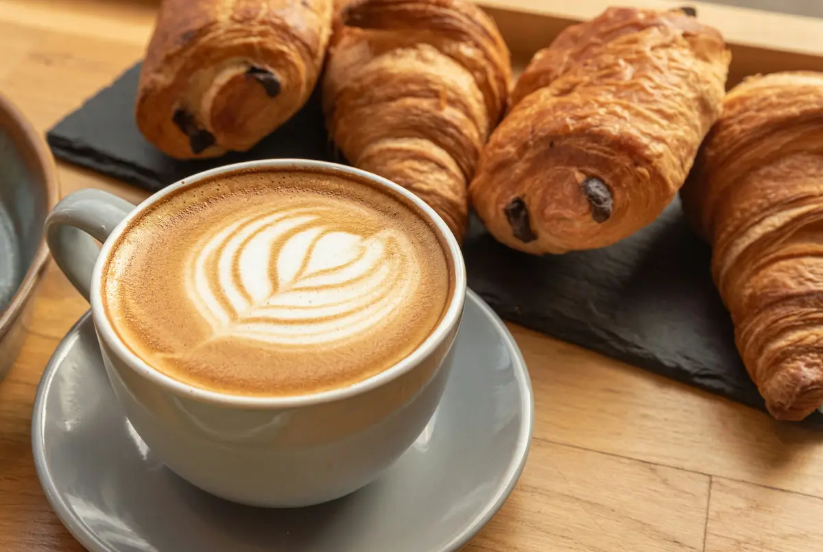 A latte with leaf art next to pains au chocolat on a wooden table